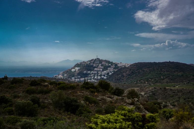 a mountain with buildings in the distance under a cloudy sky