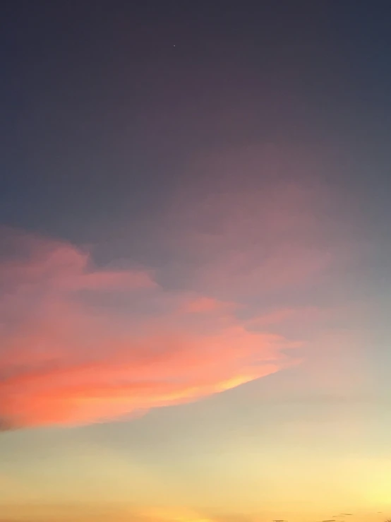 an orange and pink cloud hangs in the sky at sunset