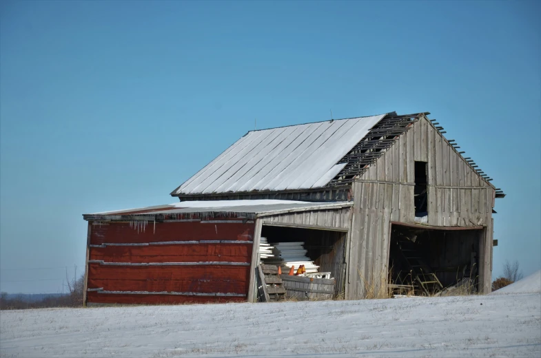 an old barn is covered with snow, and has a rusted shed