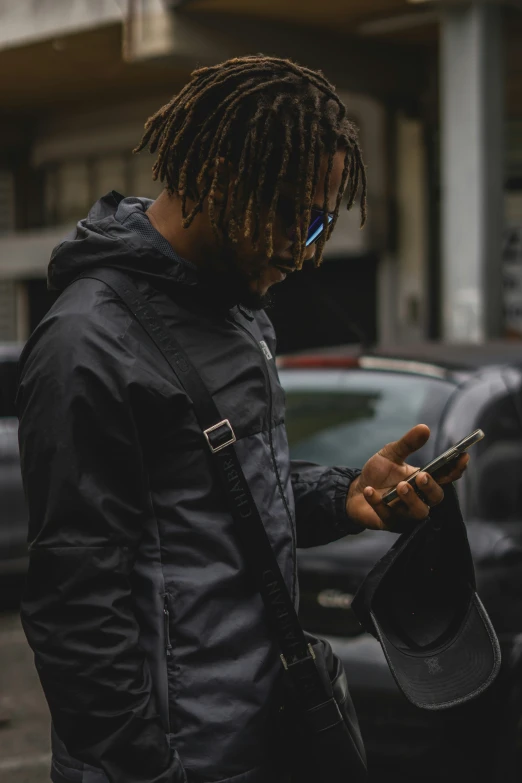 a man with dreadlocks and backpack looks at his cell phone
