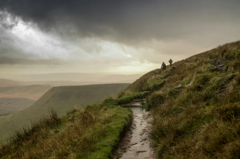 people hiking up a grassy hill near a stream