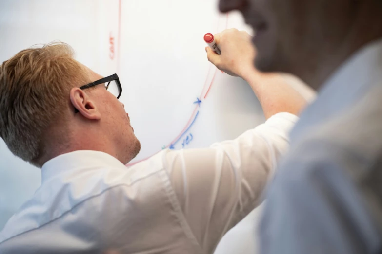 two men, one writing on a wall, another drawing on the whiteboard