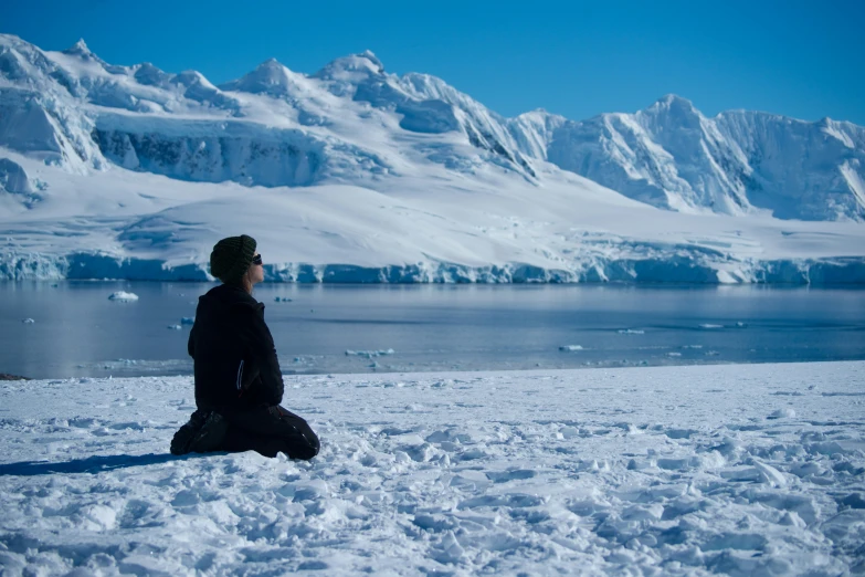 a person sitting in the snow with a view of mountains and a lake