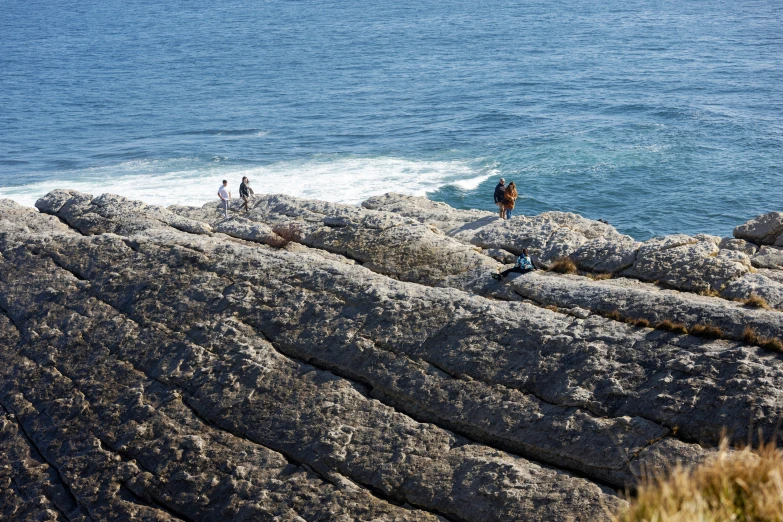 three people walk along a rocky cliff overlooking the ocean