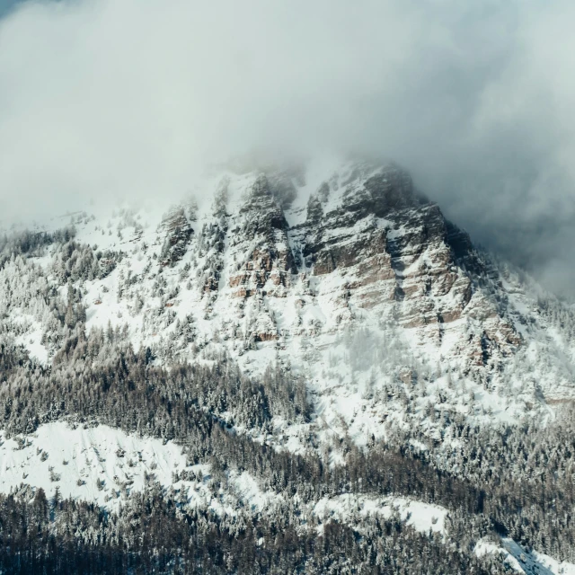 a snowy mountain with evergreens, snow, and clouds