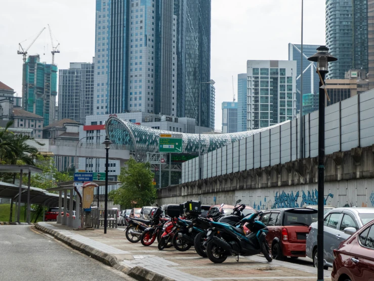 many cars and motorcycles parked next to each other on the sidewalk