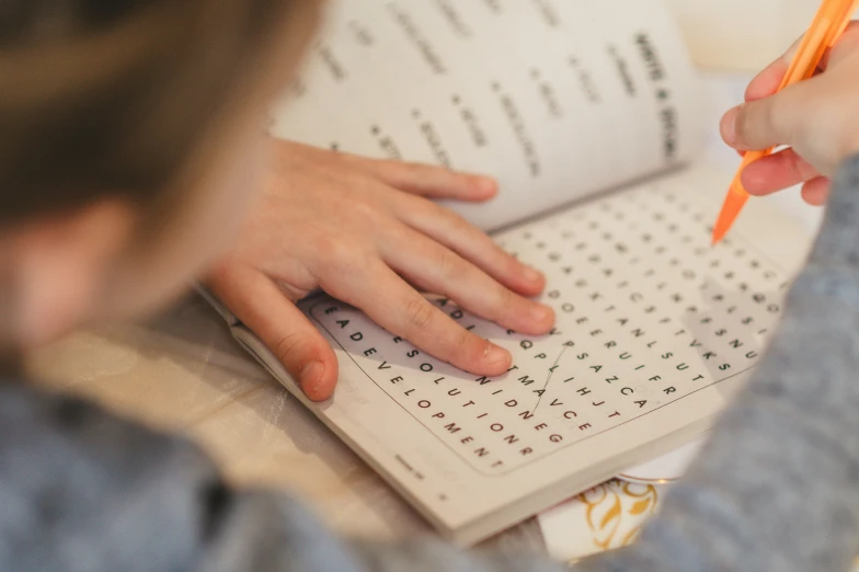 a person is writing with orange crayons on an activity book