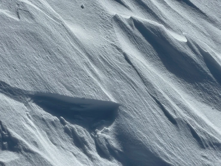 a snowy slope with several ridges, snow and one lone person in the distance