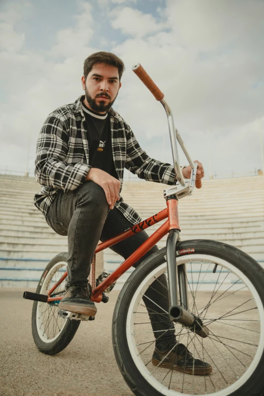 man sitting on an orange bike in front of a bleacher