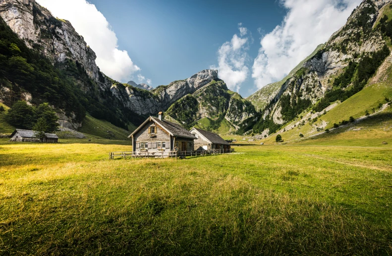 a cabin in a field with mountains and clouds