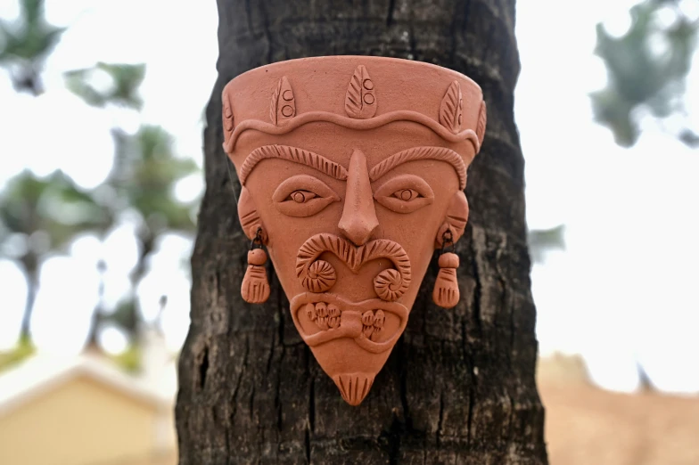 a brown mask hanging on a tree trunk