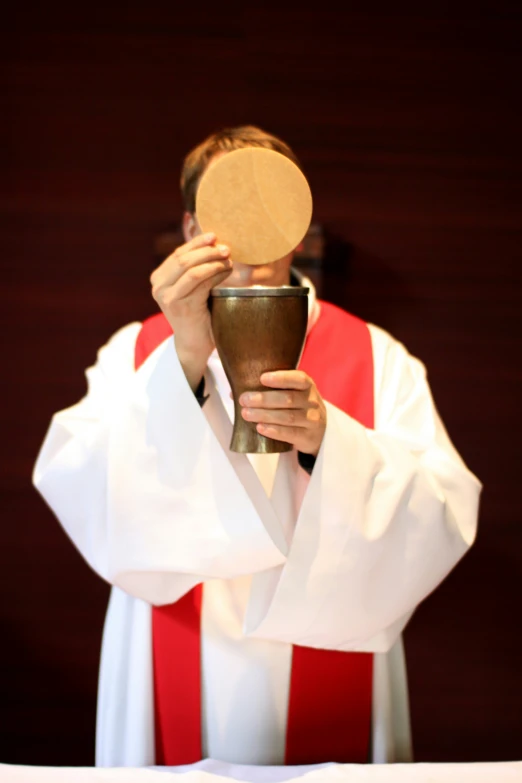 a priest covers his face with his chalice