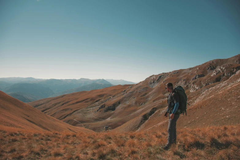 a man stands on the edge of a grassy mountain slope