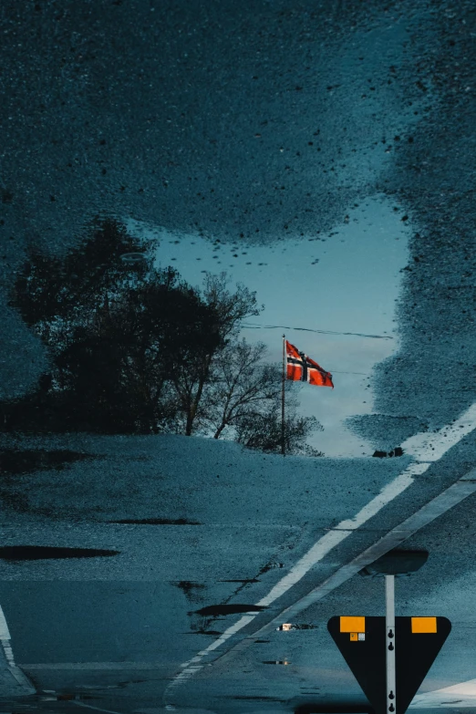 a crosswalk and a red and white flag reflected in the wet pavement