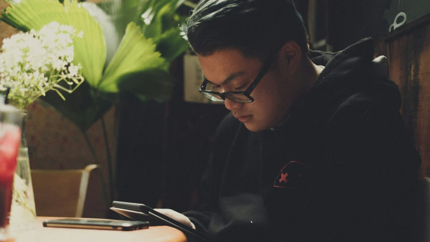 a man wearing glasses sitting at a table looking at his phone