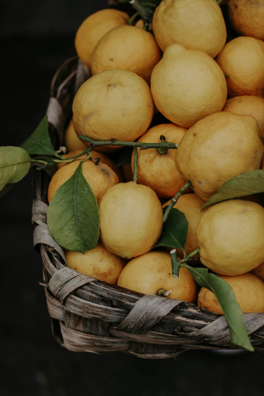 several yellow lemons sit in a basket and some leaves are on top