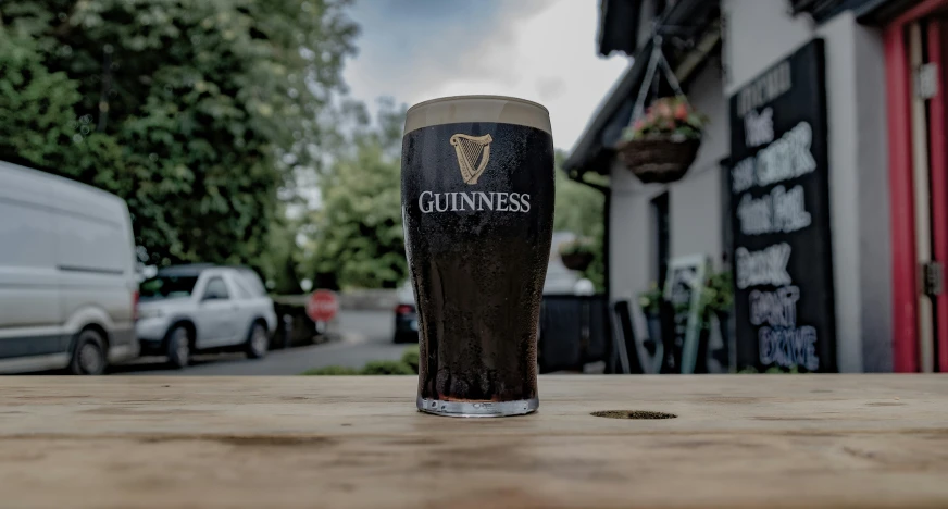 a pint glass sitting on top of a wooden table next to some trees