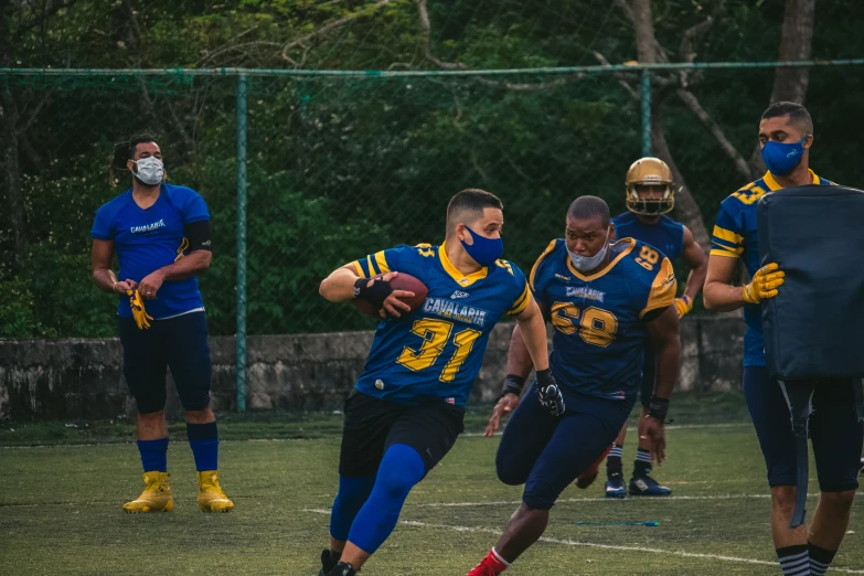 a football team in their blue and yellow uniforms with masks on and one player wearing a blue face mask