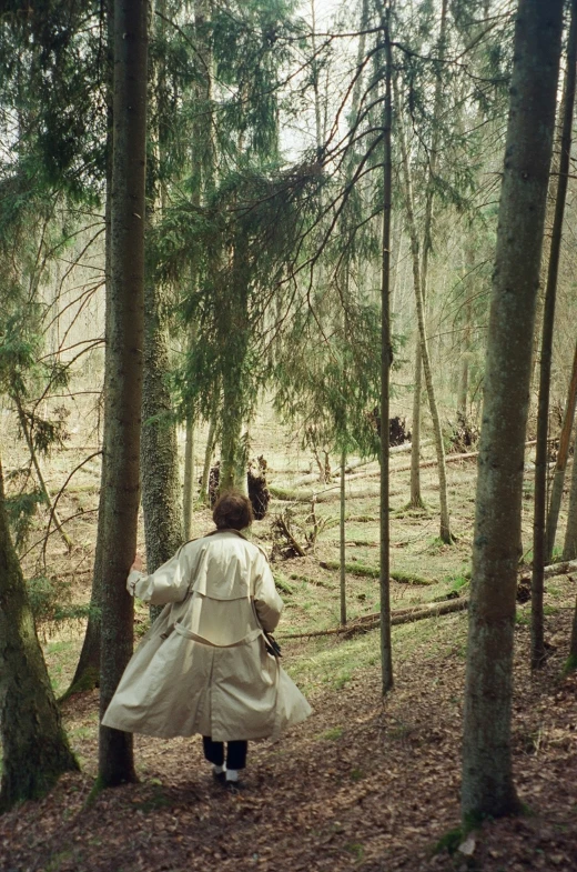 a woman in a coat walking through the woods