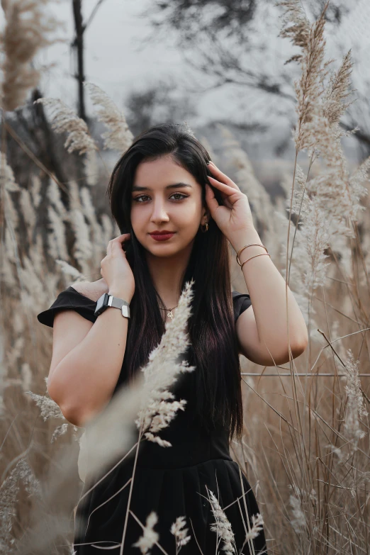 a girl is standing in tall grass holding her hands behind her head