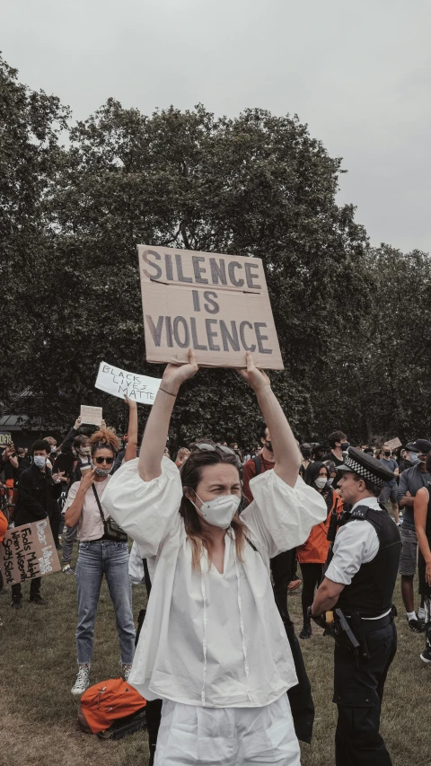 a woman wearing a mask holding up a sign that reads violence is violence