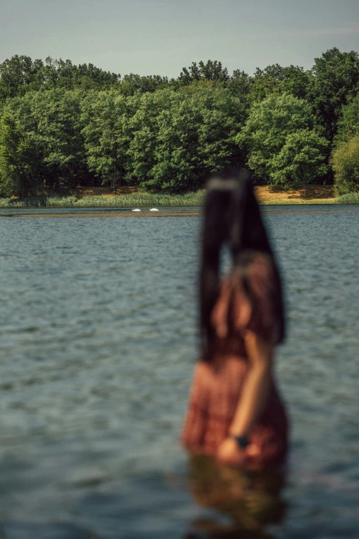 a woman standing in the water looking up at trees