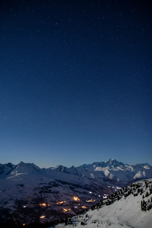 starry night sky over snow capped mountains with ski slopes