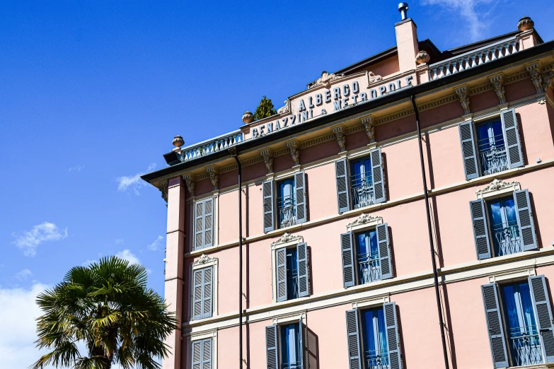 a large pink building with shutters and trees on a sunny day