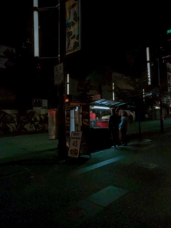 a person stands on a sidewalk with his cell phone next to the pole