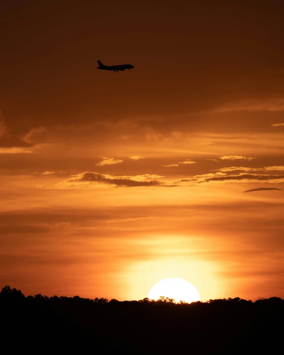 a plane flying over a sunset with a hazy sky