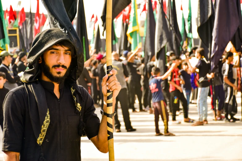 man with black mask and hood holding a large stick during a marching parade