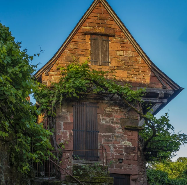 an old stone building with a wooden window surrounded by bushes