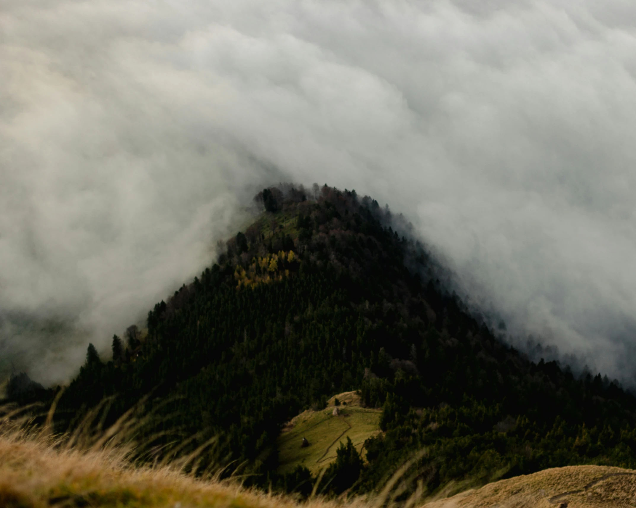 several hills and trees on the side with clouds coming off the top