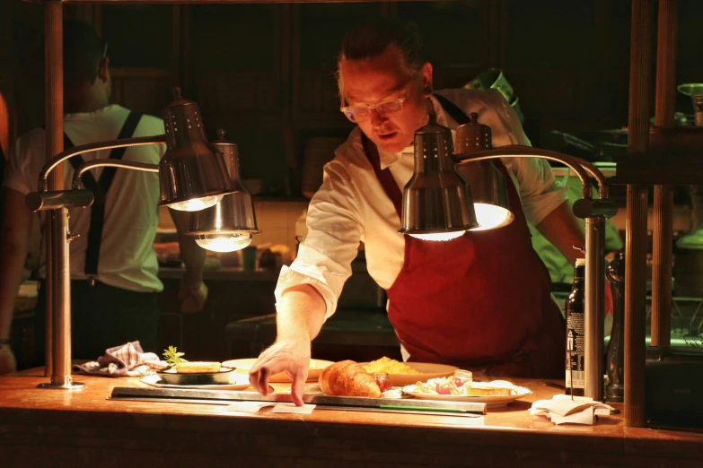 a man standing behind a counter slicing meat with utensils