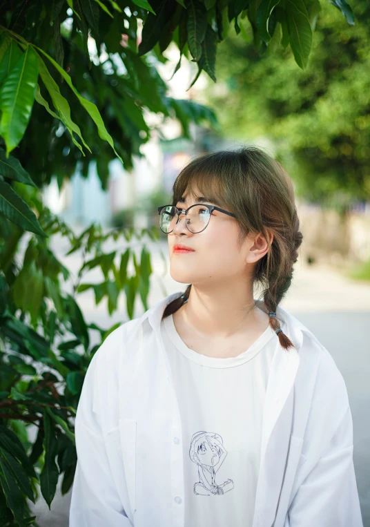 a woman wearing glasses and white shirt underneath green leaves