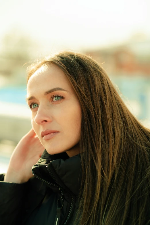 woman with long hair wearing a jacket next to water