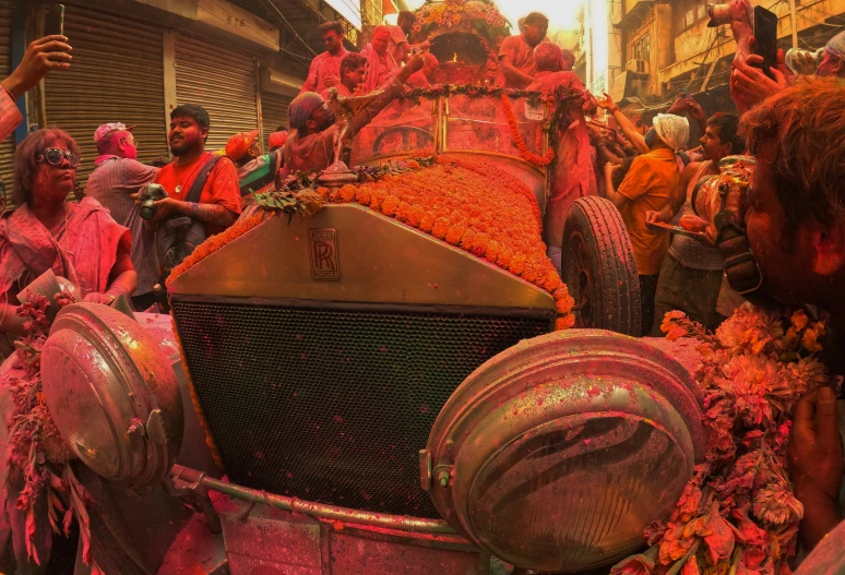 a crowd watches as a man is dressed in a car covered with flowers