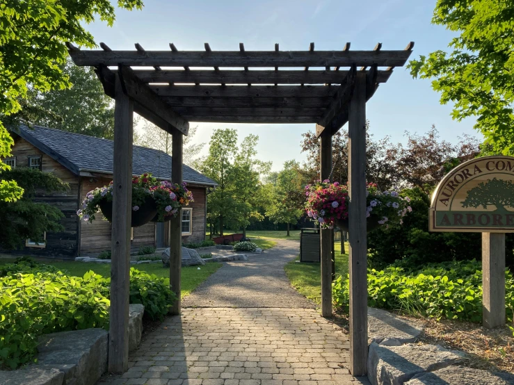 an arbor covered walkway with signpost and landscaping