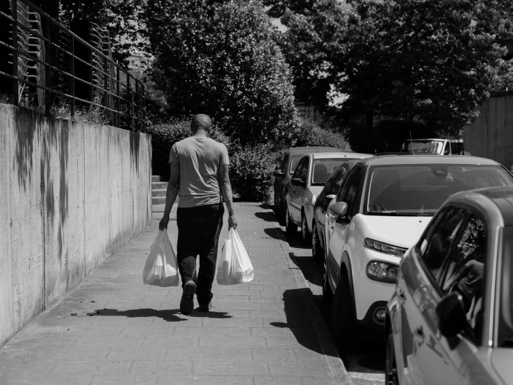 black and white pograph of a man walking down a sidewalk carrying bags