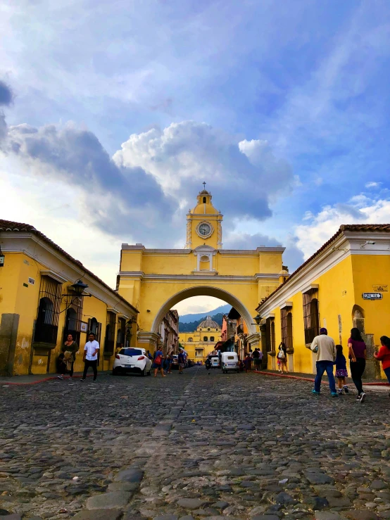 people are walking in front of yellow buildings and an arch