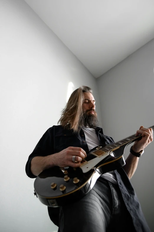 man playing a guitar indoors while wearing a black coat