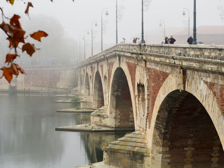 several people standing on a stone bridge over water