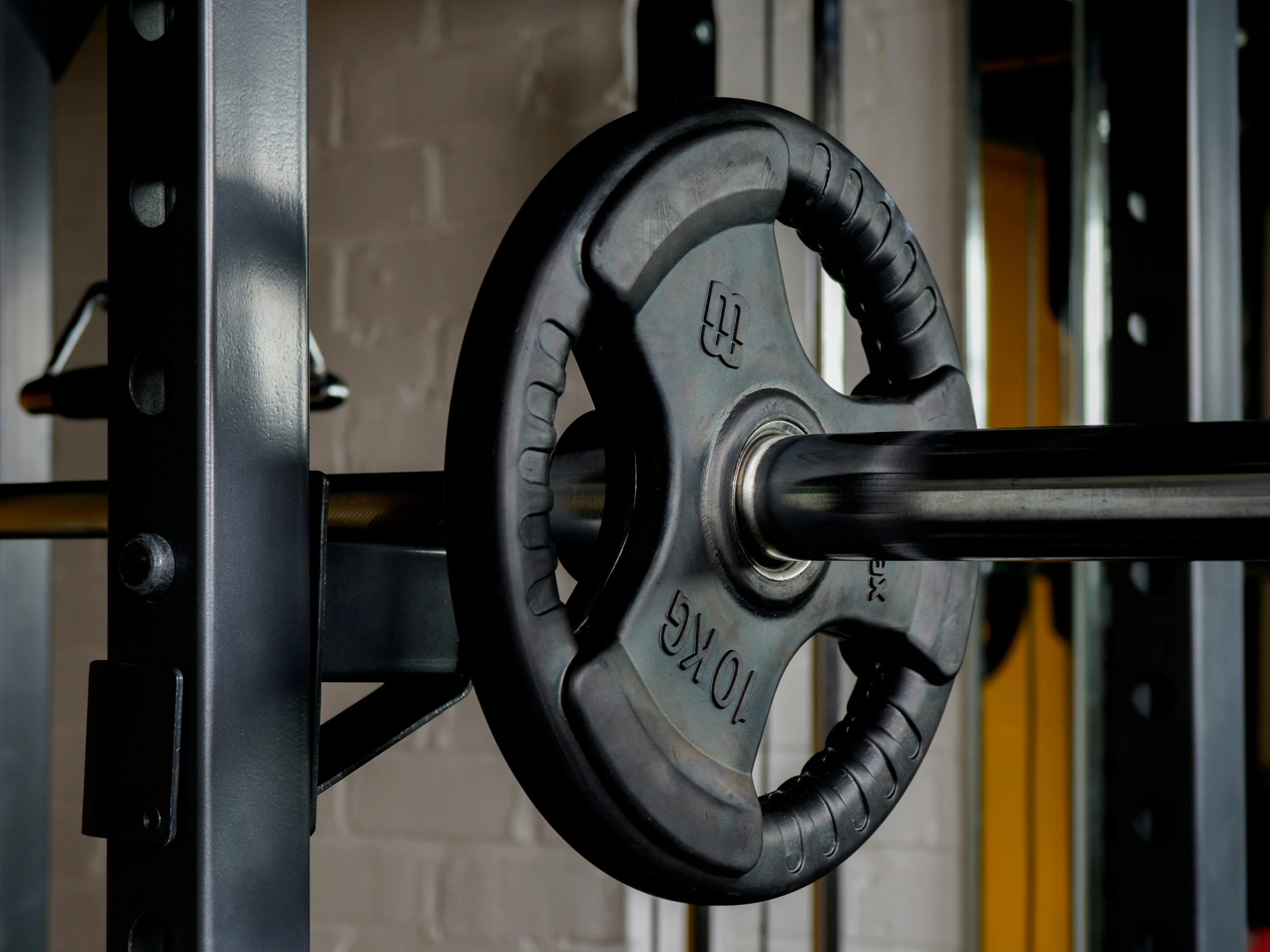 the view of a steel bar and barbell, with a large black piece of metal behind it