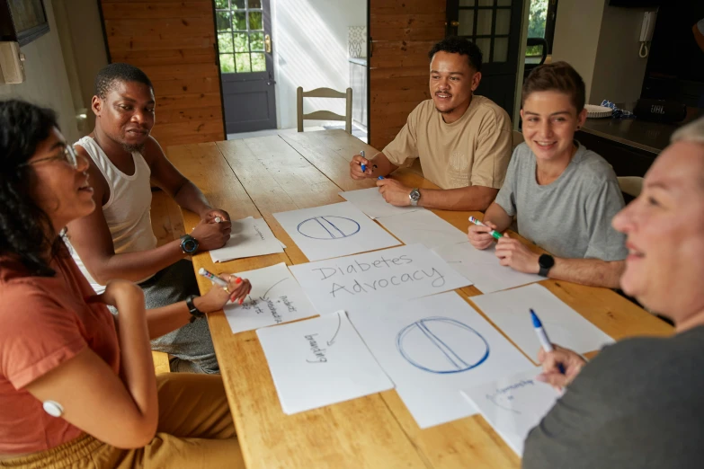 five people sitting at a table drawing shapes on paper