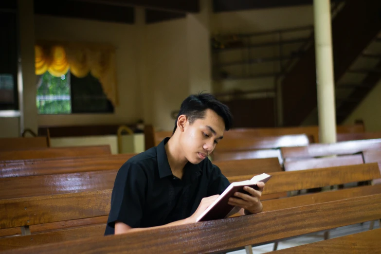a man is sitting in the pew of a church reading a book
