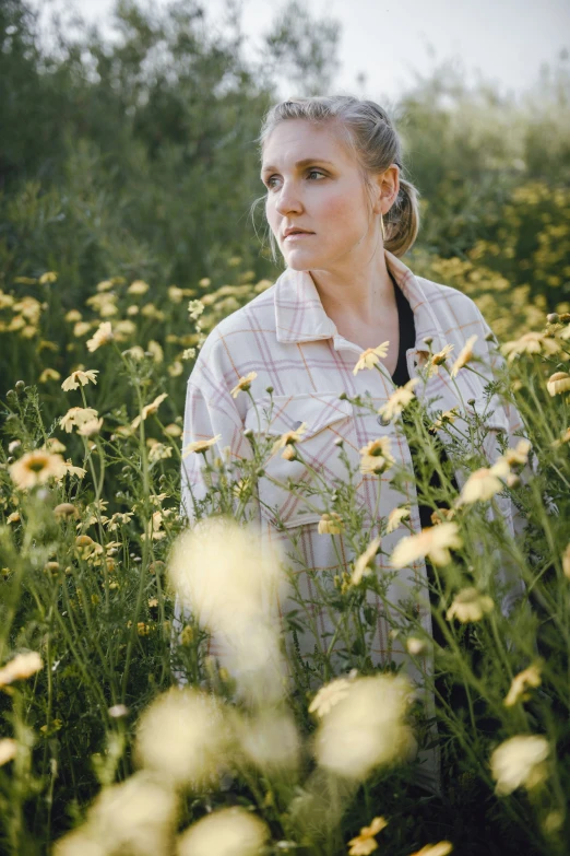 a woman standing in a field of flowers with trees in the background