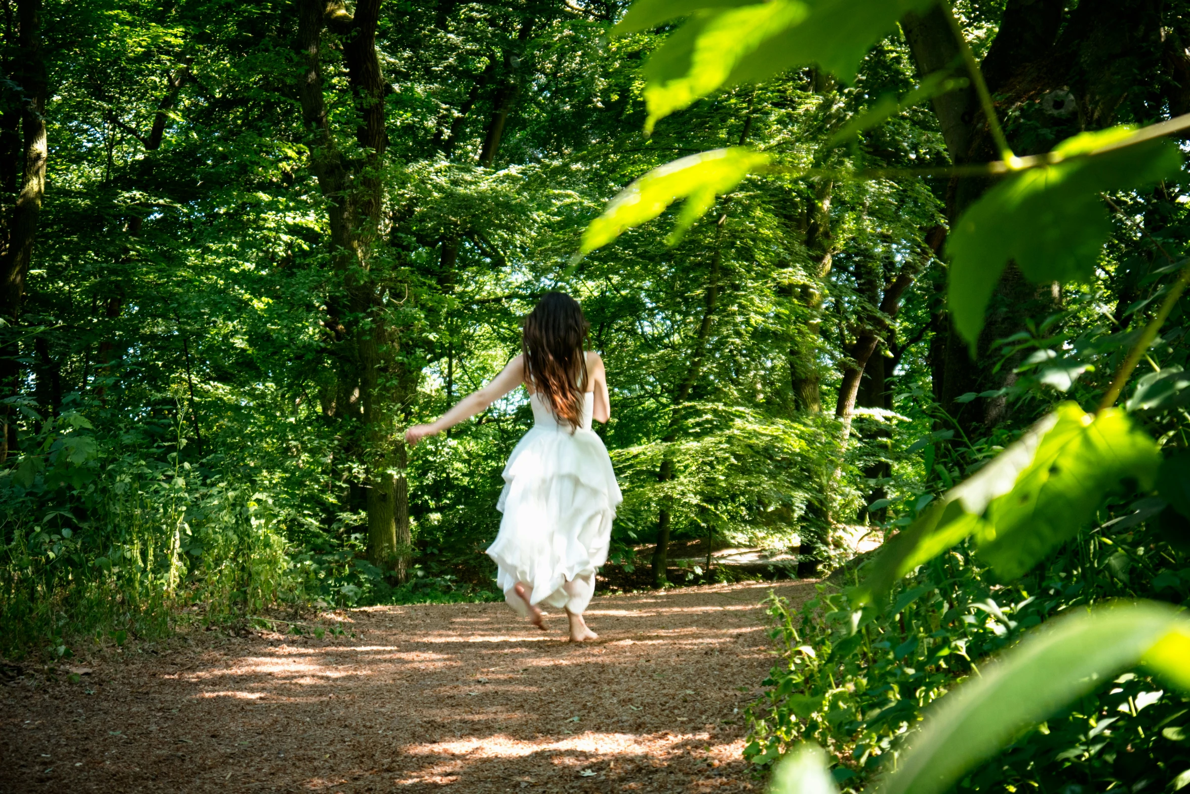 a woman with long white dress walking on a path through the woods