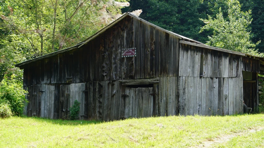 an old, broken down barn sits on a hillside with trees in the background