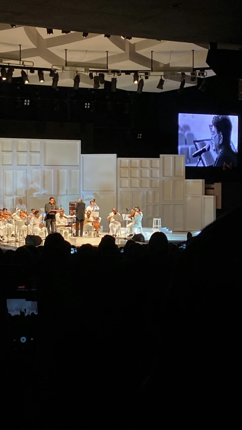 band performing on stage in darkened room with large window