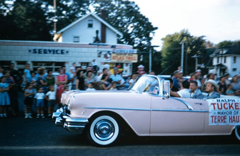 a man rides a pink car in front of a crowd